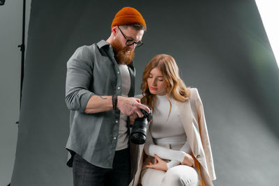 A man is holding a camera next to a woman sitting on a chair