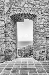 Stone wall by sea against sky seen through window