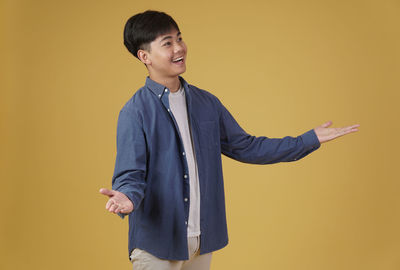 Young man looking away while standing against yellow background