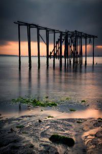 Silhouette wooden posts on beach against sky during sunset