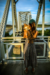 Rear view of woman with umbrella standing against railing