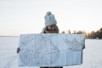 Woman holding up a map whilst standing on a frozen lake in winter