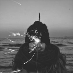 Girl holding sparkler against sea