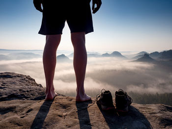 Low section of man standing on rock against sky