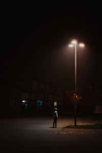 Rear view of man walking on illuminated street at night