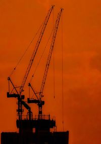 Low angle view of silhouette cranes against orange sky