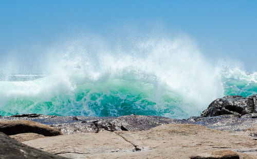 Waves splashing on rocks against sky