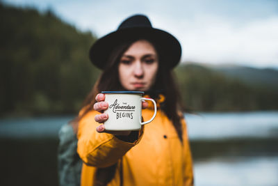 Portrait of young woman holding cup against lake