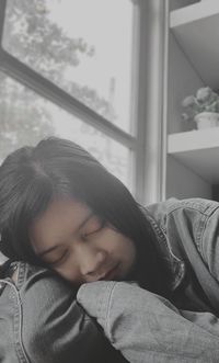 Portrait of beautiful young woman looking through window at home