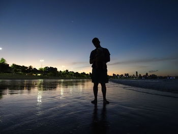 Rear view of silhouette man standing in water against sky