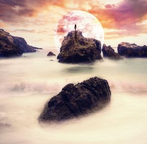 Rocks in sea against sky during sunset