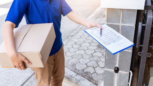 Midsection of delivery person holding cardboard box and clipboard