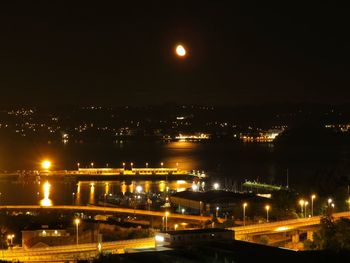 Illuminated city by river against sky at night