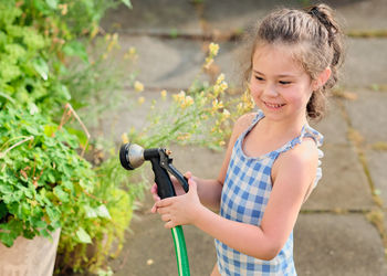 Young girl is watering plants in the backyard while wearing a bathing suit