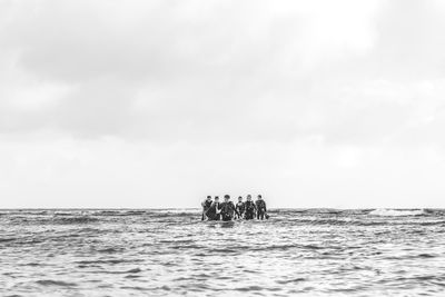 Mid distance view of scuba divers walking in sea against sky