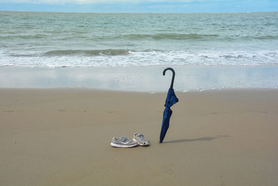 A closed umbrella is stuck in the sand and old shoes with holes stand on the beach 