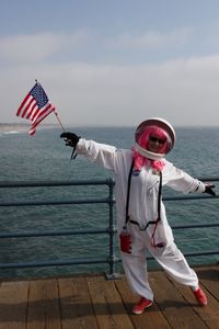 Portrait of mid adult woman in space suit standing on pier over sea against sky