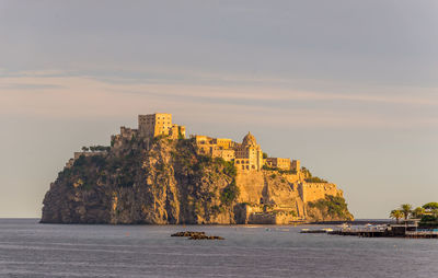 Low angle view of buildings on mountain by sea against sky