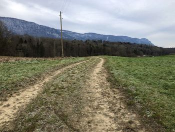 Dirt road amidst field against sky