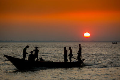 Silhouette people in river against sky during sunset