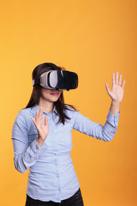 Portrait of young woman standing against yellow background