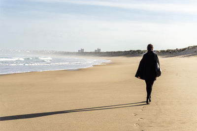 Rear view of woman walking at beach against sky