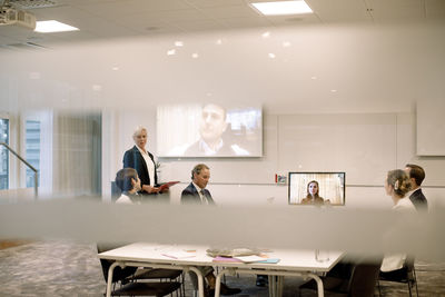 Male and female executives discussing in web conference meeting seen through glass at workplace