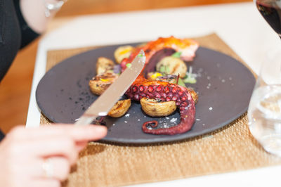 Midsection of person eating tentacles served on table at restaurant