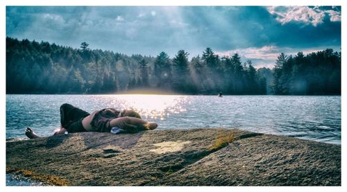 Panoramic view of young woman relaxing on rock at lakeshore