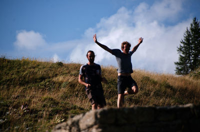 Rear view of young adult with arms raised standing on field against sky