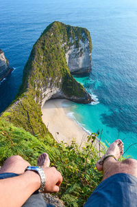 Low section of man sitting on cliff against sea