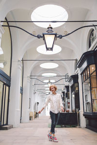 Happy woman standing on tiptoe in illuminated arch corridor