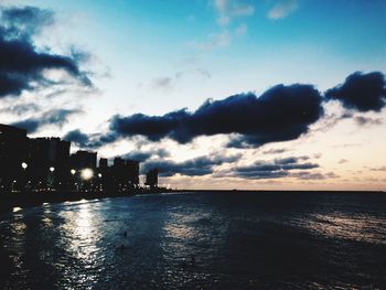 Scenic view of sea by buildings against sky at sunset