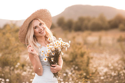 Portrait of smiling woman holding flowers in field