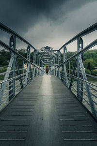 Man walking on footbridge against sky