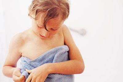 Boy wrapped in towel standing against wall at bathroom