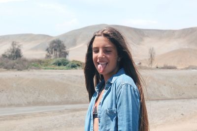 Young woman sticking out tongue while standing on landscape