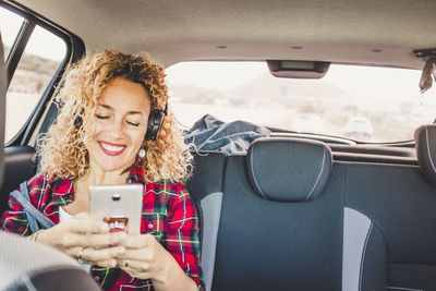 Smiling woman using smart phone sitting at car