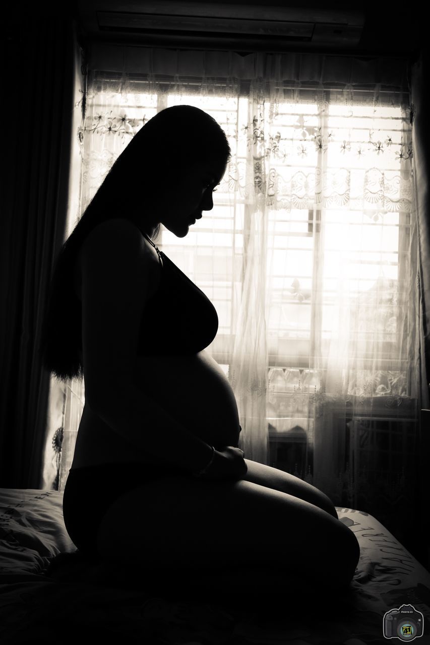 SIDE VIEW OF WOMAN SITTING AT WINDOW