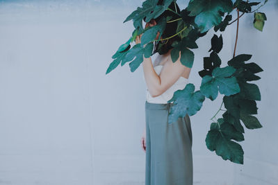 Close-up of mature woman hiding behind plant against wall