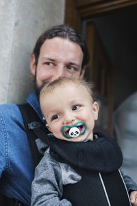 Mid adult man carrying baby boy in carrier at doorway