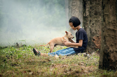 Side view of girl sitting with dog at forest