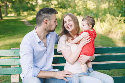 Caucasian smiling laughing mother and father with baby daughter in park. happy family mom, dad, kid