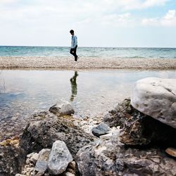 Full length of man on rocks at beach against sky