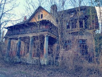 Low angle view of abandoned house against bare trees