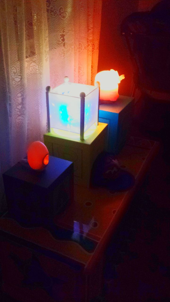 indoors, illuminated, home interior, wall - building feature, close-up, table, red, light - natural phenomenon, multi colored, candle, childhood, human representation, dark, creativity, room, glowing, communication