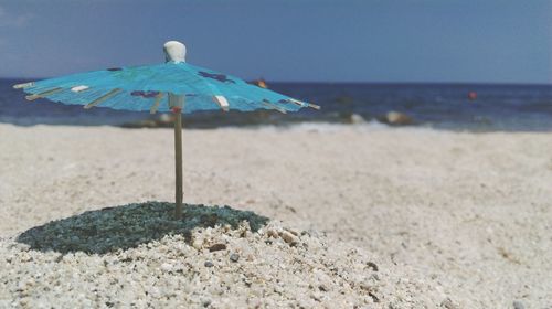 Close-up of drink umbrella on sand at beach against sky