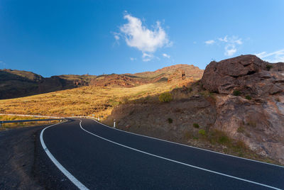 Empty road leading towards mountains against blue sky