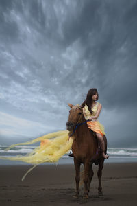 Full length of woman riding horse on beach against sky