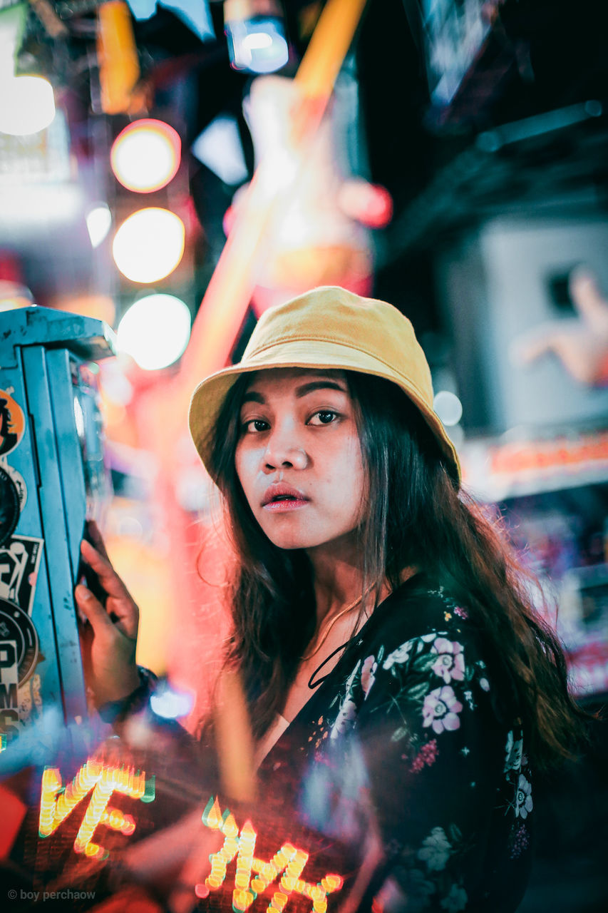 one person, real people, night, lifestyles, illuminated, women, young adult, leisure activity, portrait, young women, adult, headshot, focus on foreground, looking, hat, waist up, city, hair, hairstyle, outdoors, beautiful woman